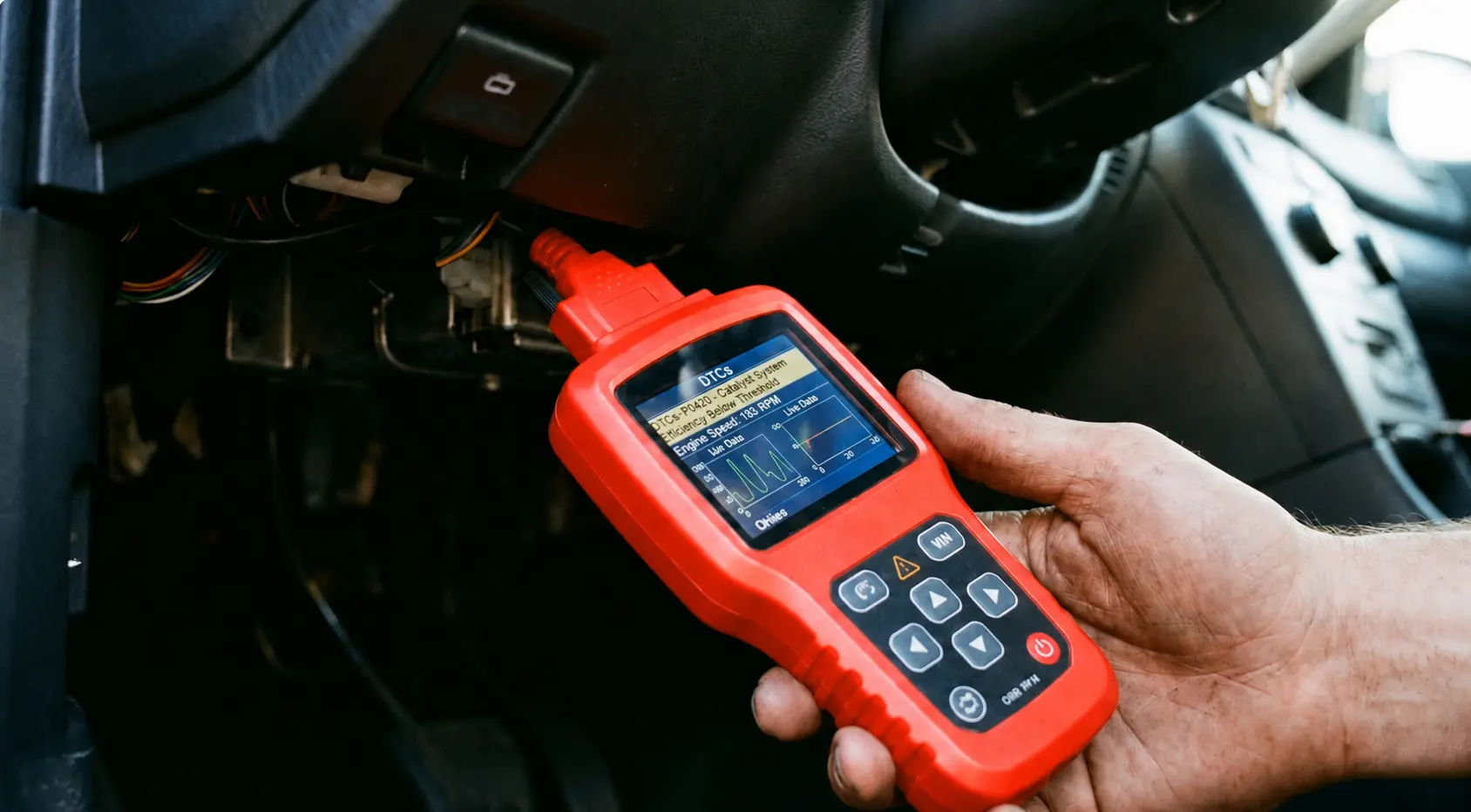 OBD-II scanner plugged into a car diagnostic port under the dashboard to read check engine light fault codes and diagnose vehicle problems.