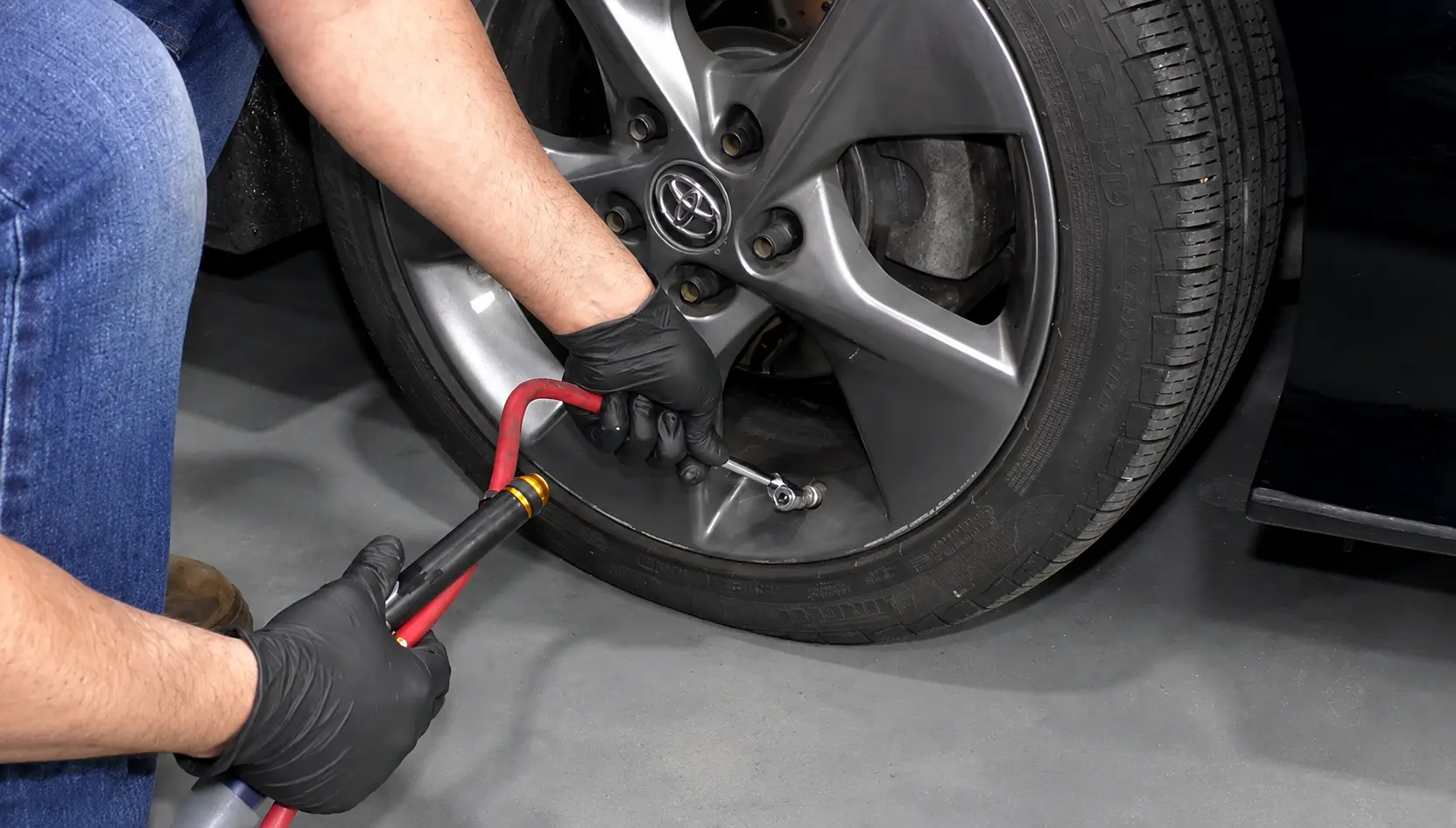 Technician checking a car tire's air pressure with a digital tire pressure gauge to ensure the correct PSI and proper TPMS operation.