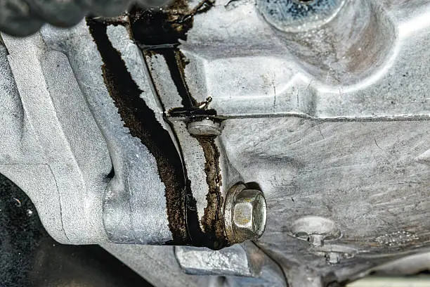 Engine oil leaking beneath a parked car indicating an oil leak that can lead to low engine oil pressure.